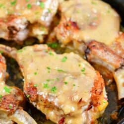 Pork chops are smothered and cooked in a large black pan.
