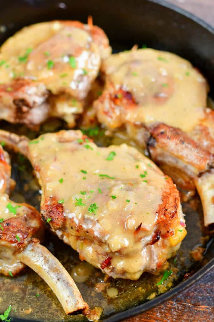 Pork chops are smothered and cooked in a large black pan.