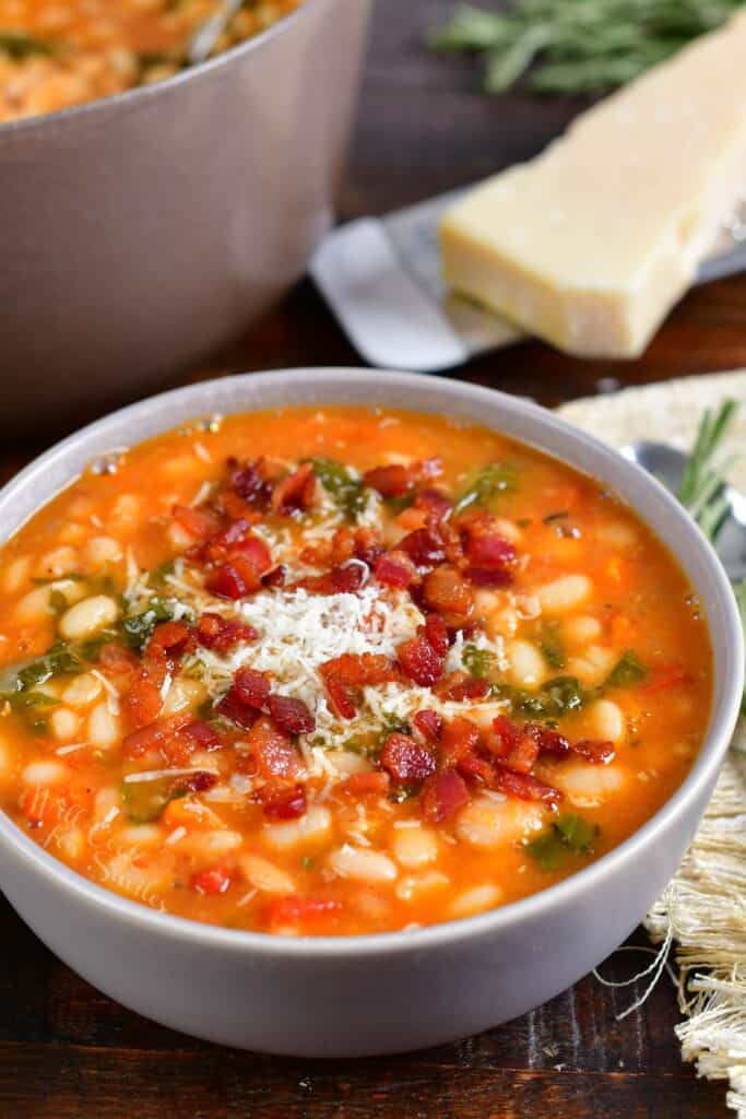 A bowl of soup is topped with parmesan and bacon bits.