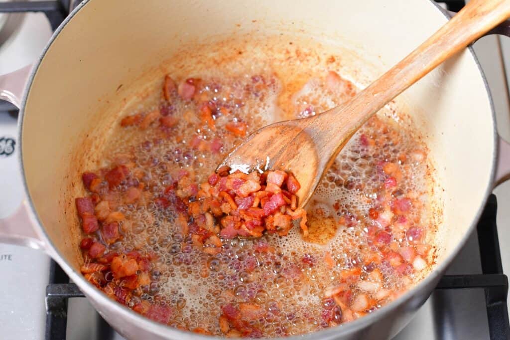 Bacon is being cooked in a dutch oven.