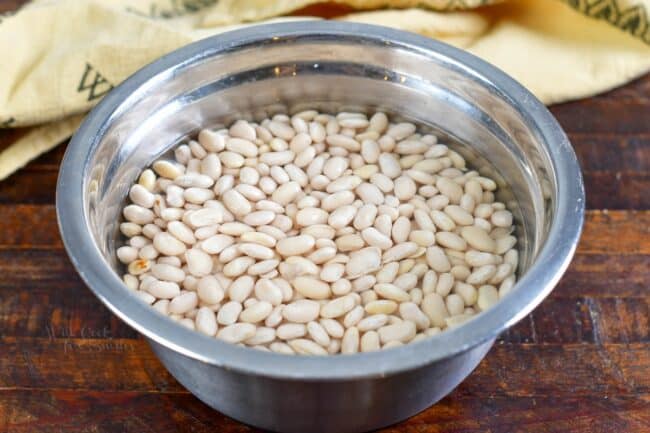 White beans are being soaked in a metal bowl filled with water.