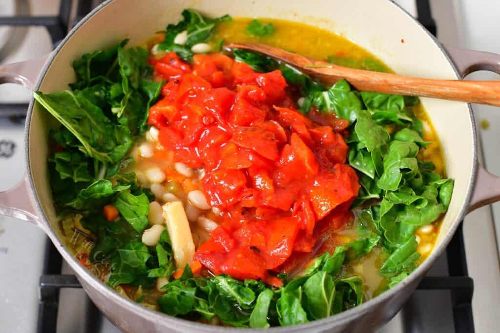 Tomatoes and leafy greens have been added to the cooking soup.