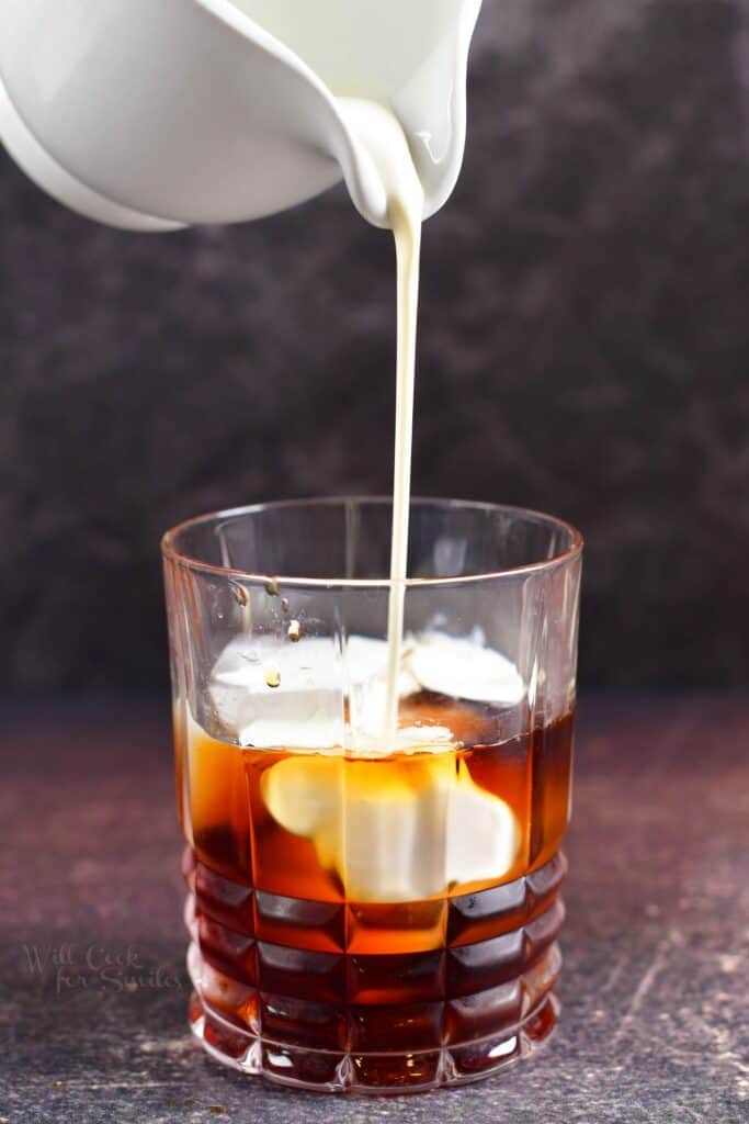 pouring in heavy whipping cream into the cocktail glass with Kahlua and vodka