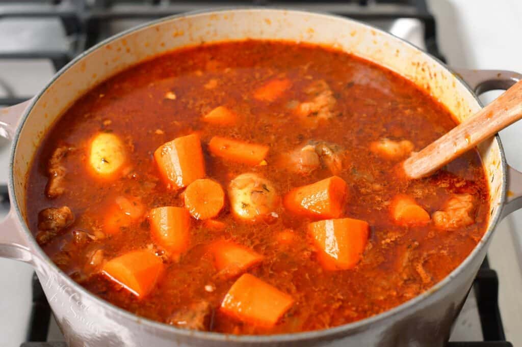 adding carrots and potatoes to the beef stew on a stove