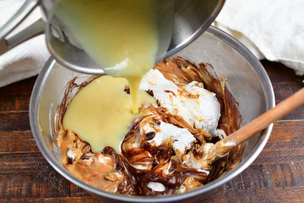 pouring in sweetened condensed milk into the bowl with chocolate and peanut butter
