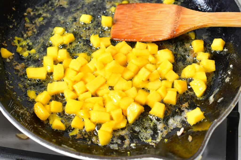 mango pieces cooking in a pan with a spatula visible