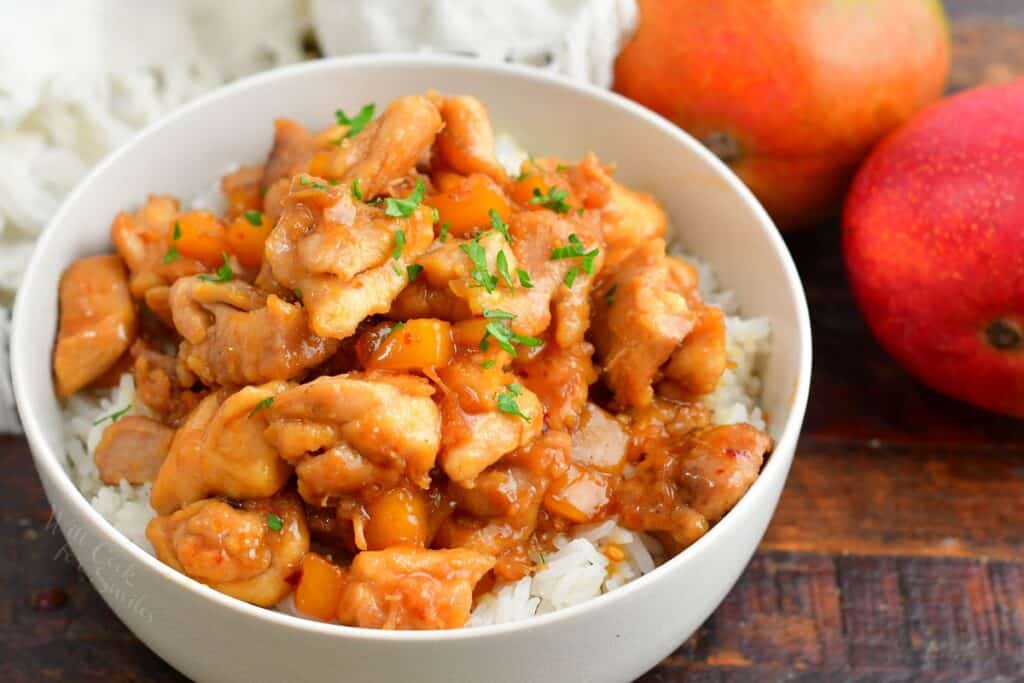 top view of mango chicken and rice in a bowl with mangoes next to it