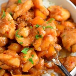 scooping some mango chicken with a fork from a bowl