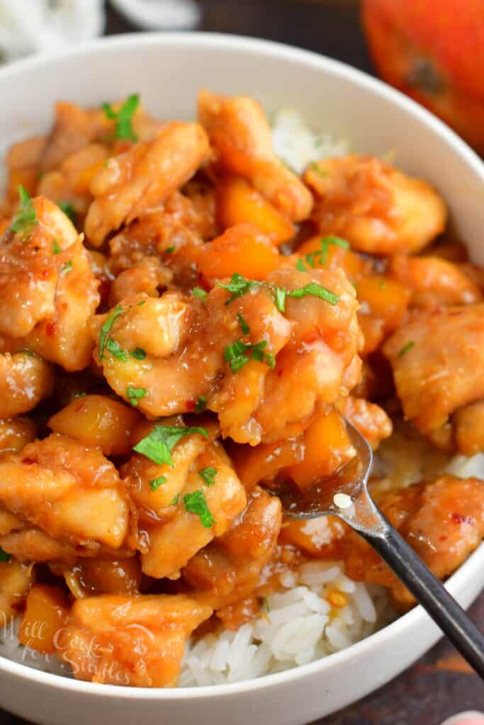 closeup of cooked mango chicken in a bowl with rice on a fork