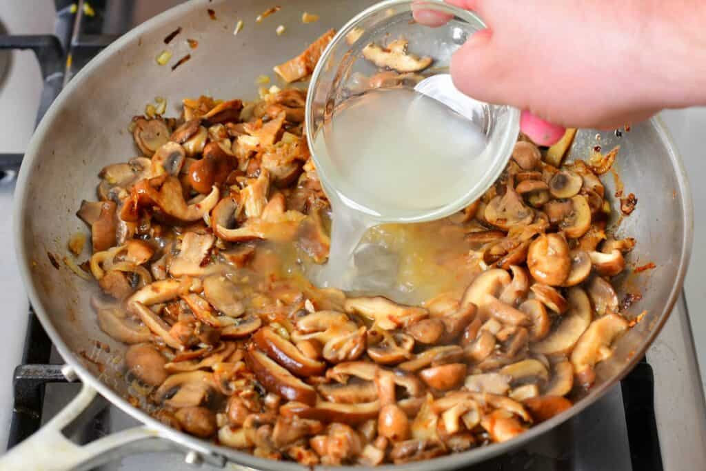 adding pasts cooking water to sautéed mushrooms in the pan