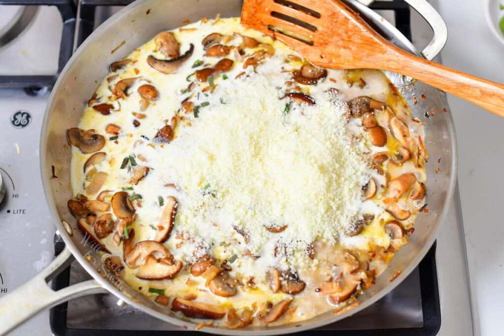 grated parmesan cheese added to the creamy mushroom sauce in a pan