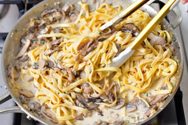 tossing cooked pasta with mushroom sauce in the pan