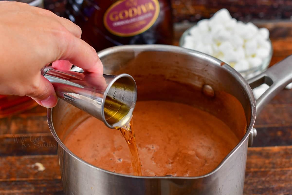 pouring in bourbon into the pot with hot chocolate.