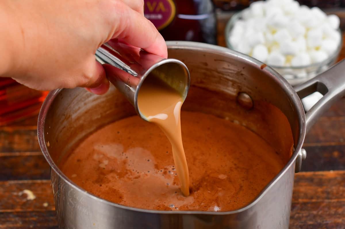 pouring in chocolate liqueur into the pot with hot chocolate.