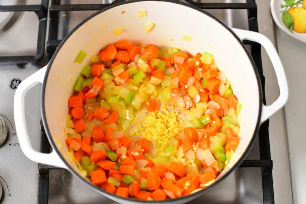 adding garlic to the sautéing vegetables in a pot