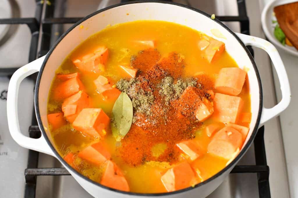 sweet potatoes covered in broth and topped with seasoning in a pot