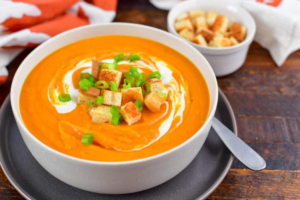 sweet potato soup in a bowl with croutons on top and next to the bowl