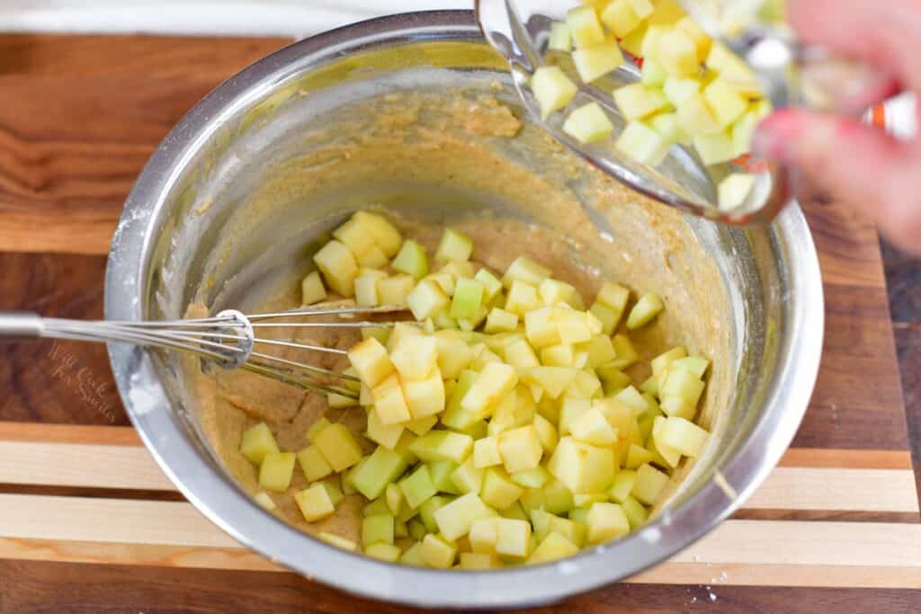 adding apples to the batter in a bowl