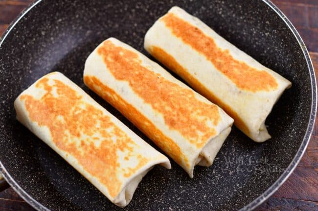 searing rolled breakfast burritos in a pan