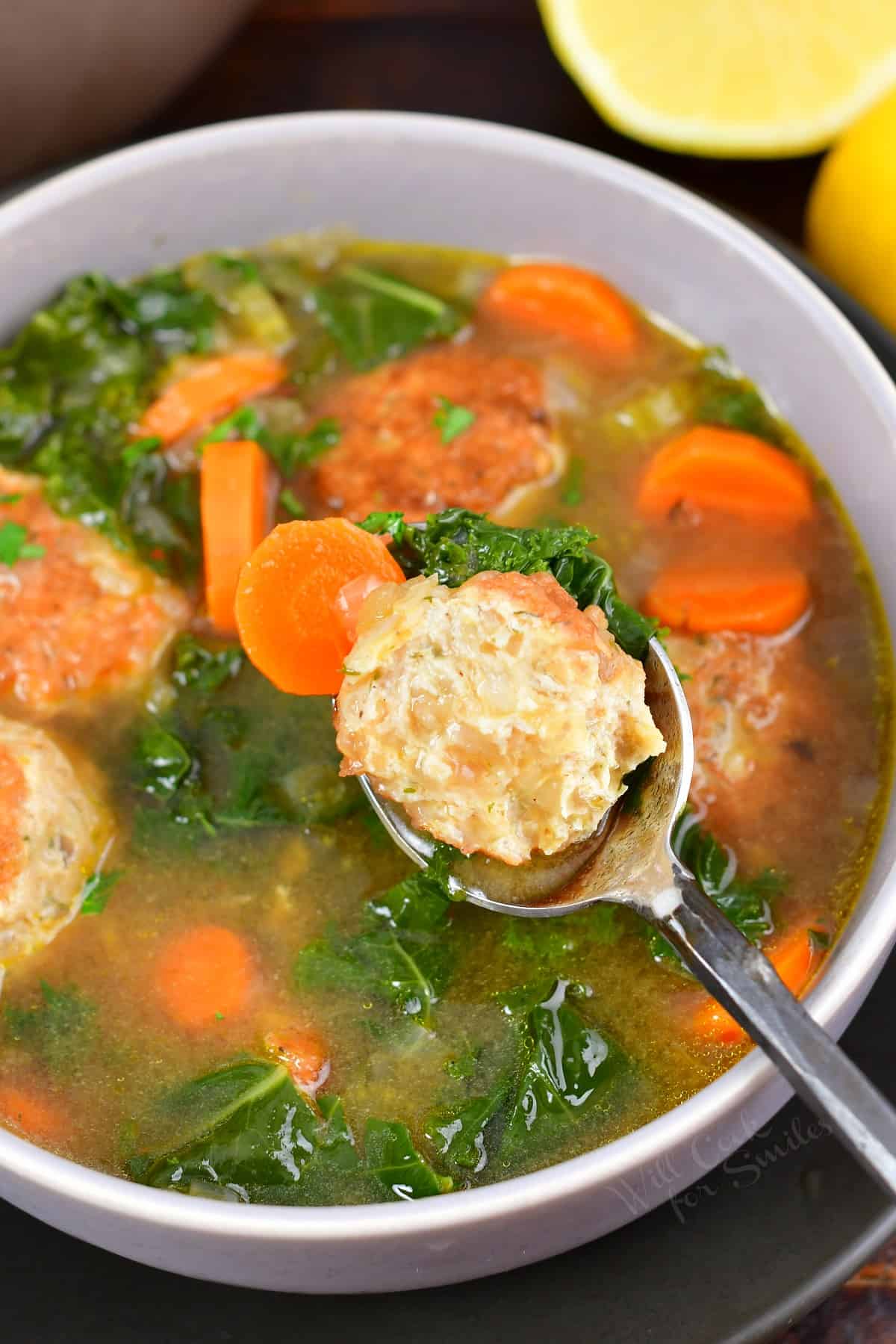 spoon with half of a chicken meatball over bowl of soup