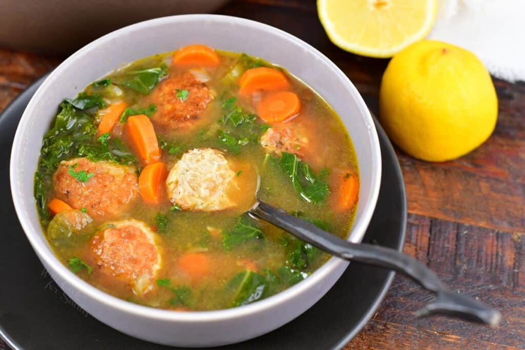 a bowl of chicken meatballs soup with a spoon and lemon halves next to it