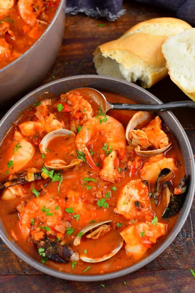 top view of Cioppino fish stew in a grey bowl with bread and a spoon