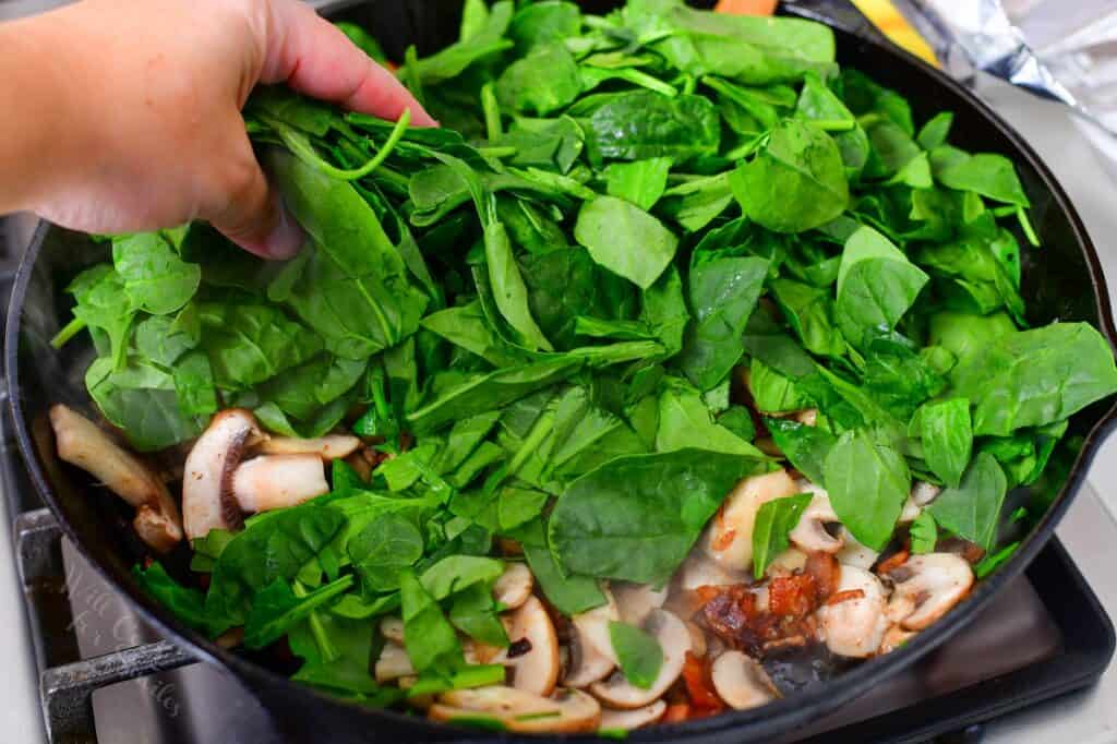 adding spinach to bacon and mushrooms in a skillet