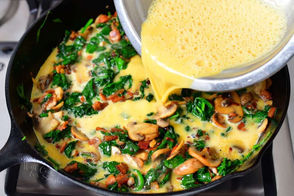 adding eggs to the cooked vegetables in a cast iron skillet