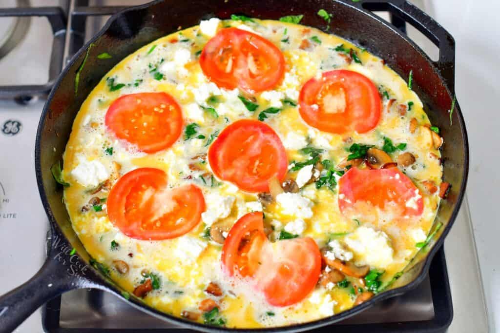 frittata ingredients in a cast iron skillet with tomatoes and feta cheese before baking