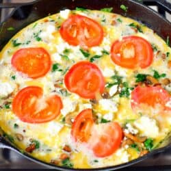 frittata ingredients in a cast iron skillet with tomatoes and feta cheese before baking