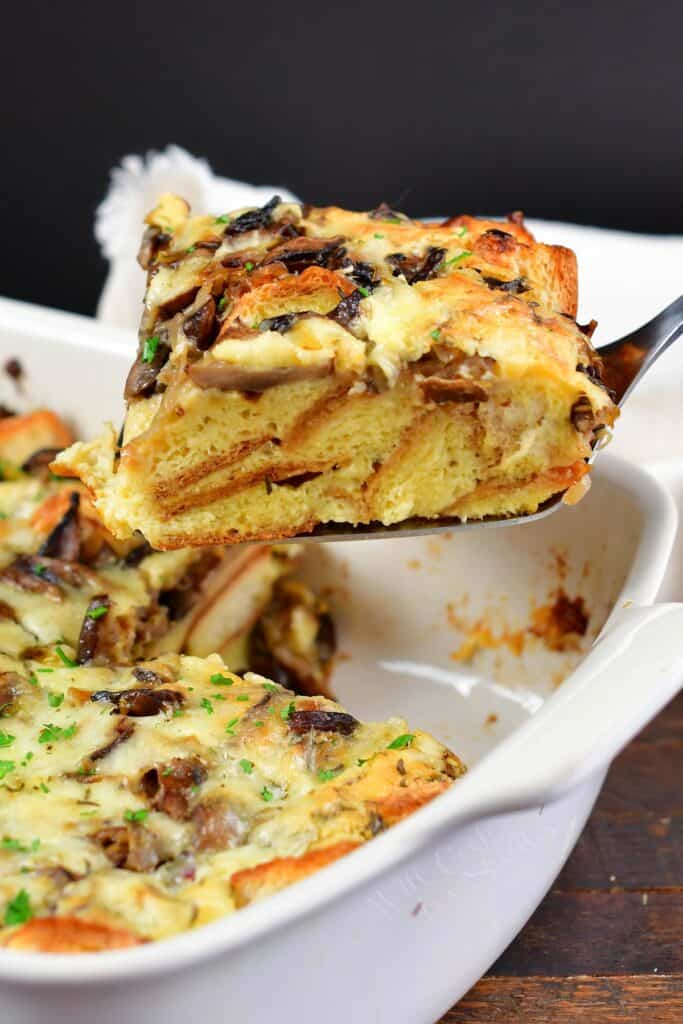 pulling out a cut slice of mushroom bread pudding from a dish