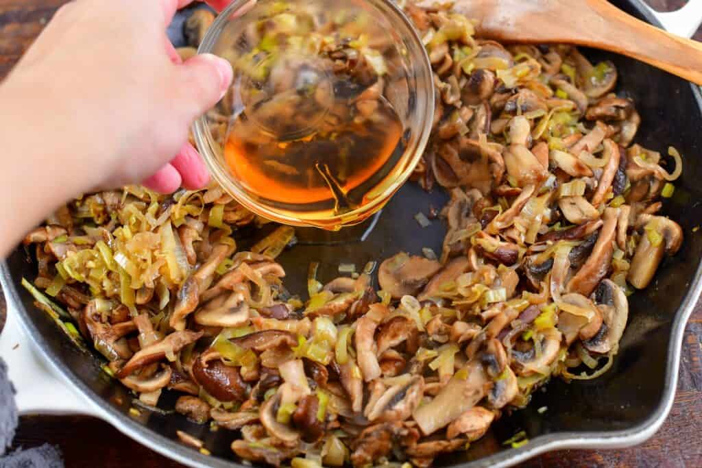 adding cognac into pan with sautéed mushrooms