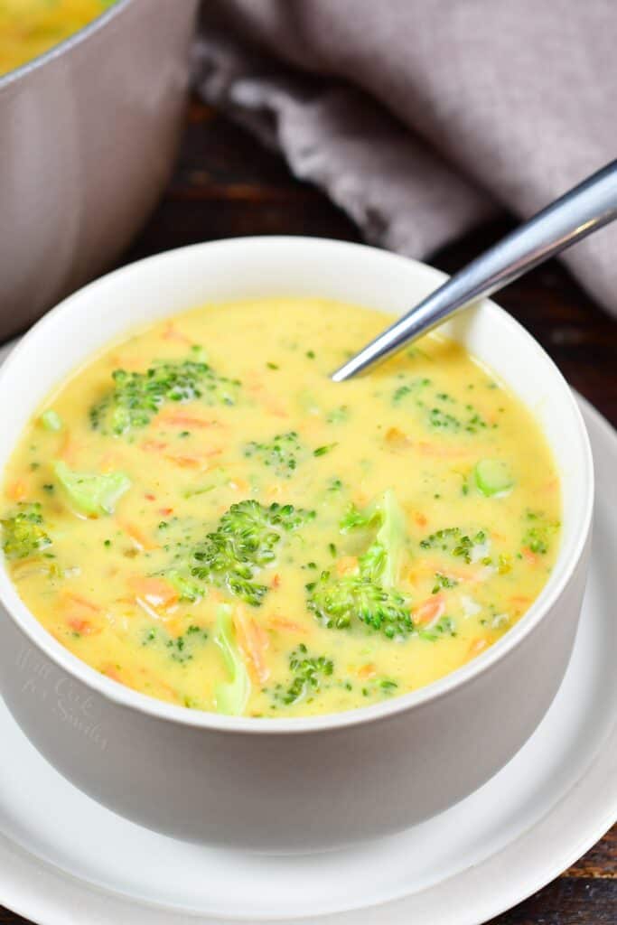 broccoli cheese soup inside a white and tan bowl on a small plate