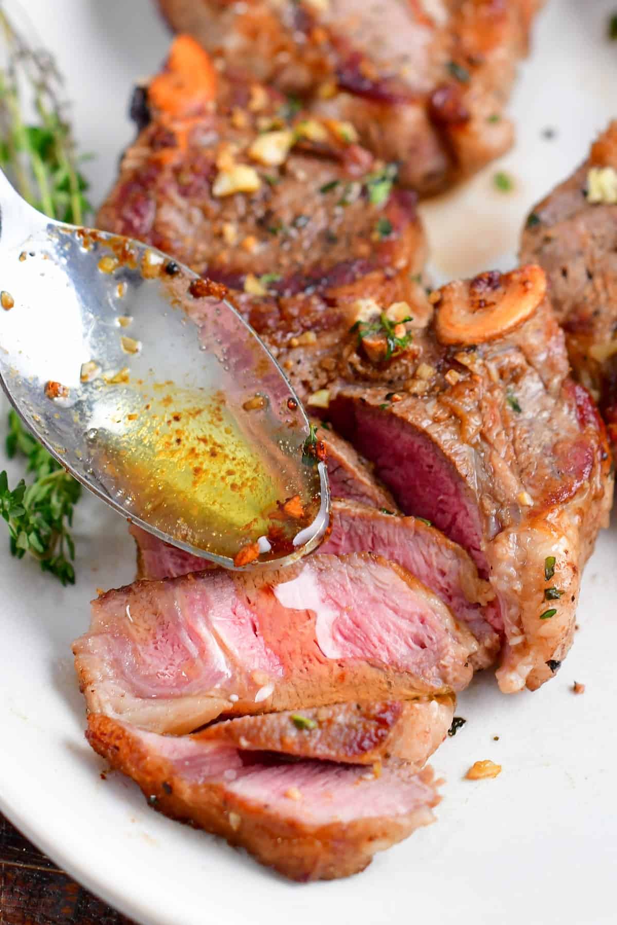 drizzling butter sauce over sliced lamb chop with a spoon.