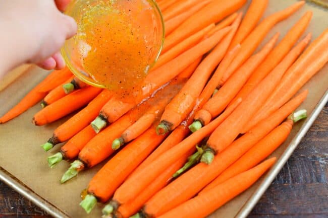 adding glaze to the whole carrots on a baking sheet