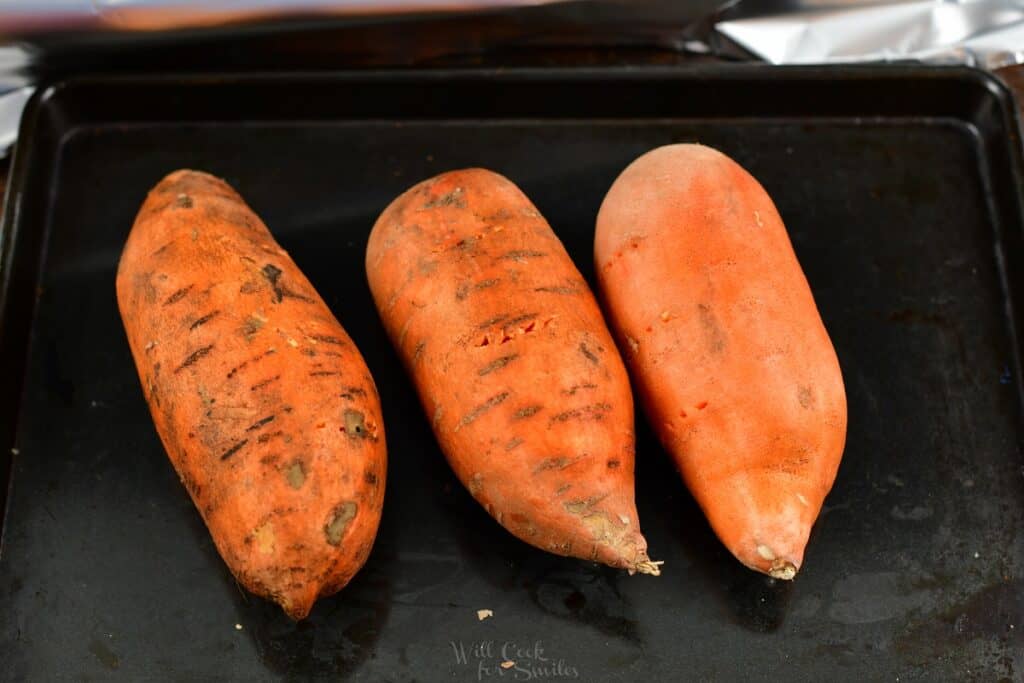 three sweet potatoes on a baking sheet with holes poked through