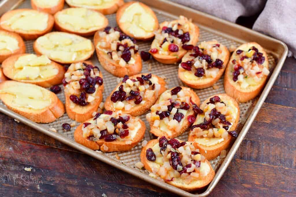 crostini on the baking sheet topped with cranberry pear