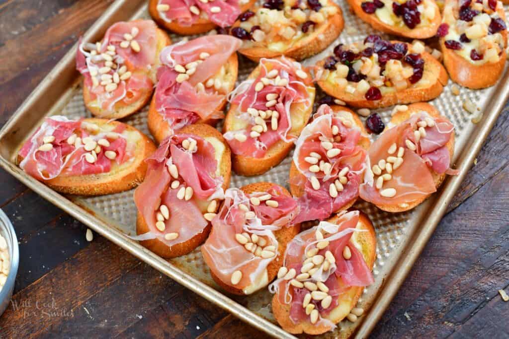 crostini on a sheet pan topped with prosciutto and pine nuts