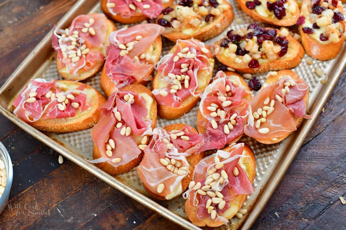 crostini on a sheet pan topped with prosciutto and pine nuts
