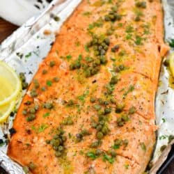 closeup of baked salmon topped with capers on baking sheet