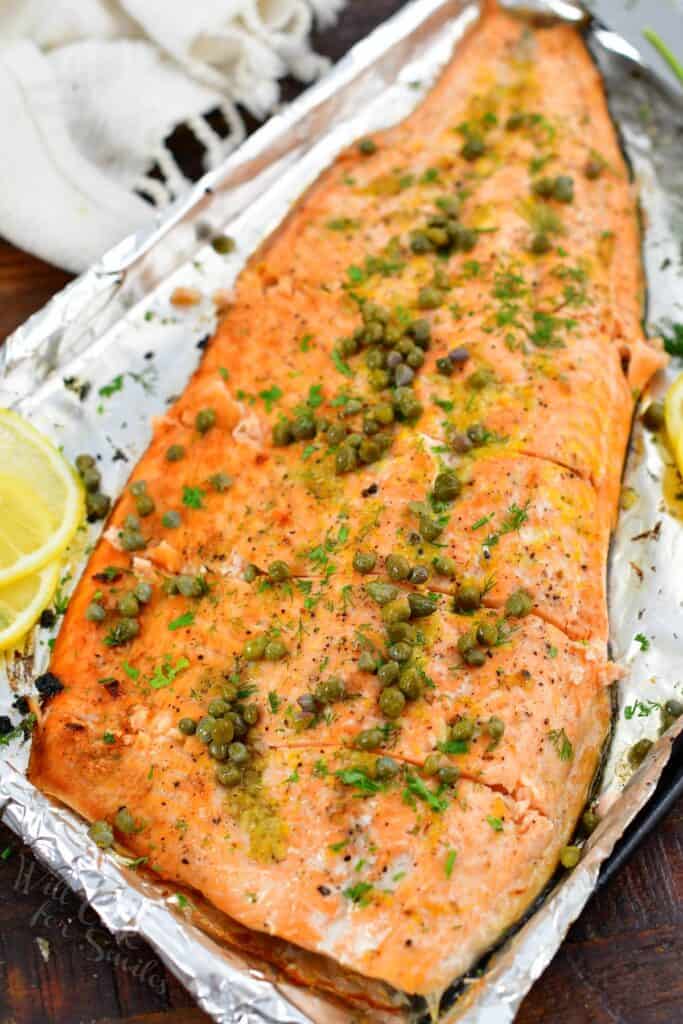 closeup of baked salmon topped with capers on baking sheet