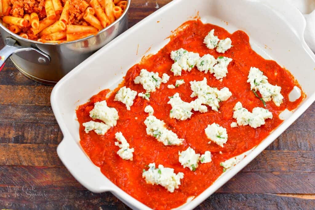 pasta sauce spread out in a baking dish with drops of ricotta