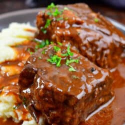 side view of short ribs on a plate with potatoes covered in sauce