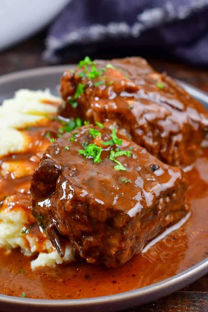 side view of short ribs on a plate with potatoes covered in sauce