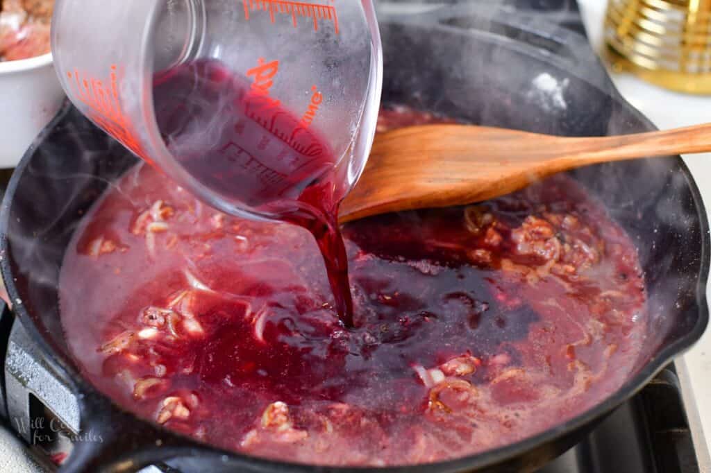 pouring in red wine into the pan with onions and garlic