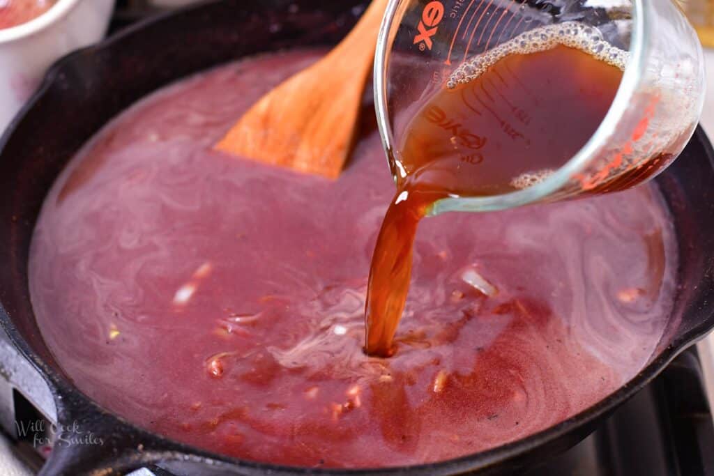 pouring in beef stock into the pan with sauce