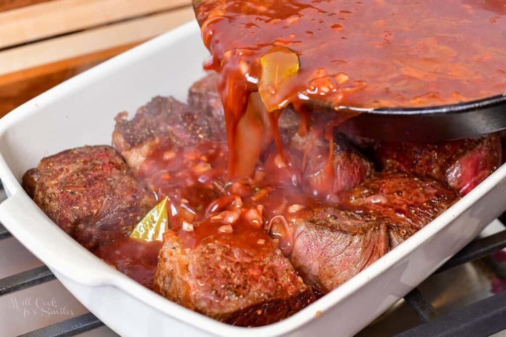pouring the sauce over the short ribs in the baking dish