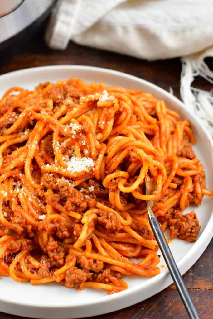 swirling pasta with meat sauce into a fork on a plate