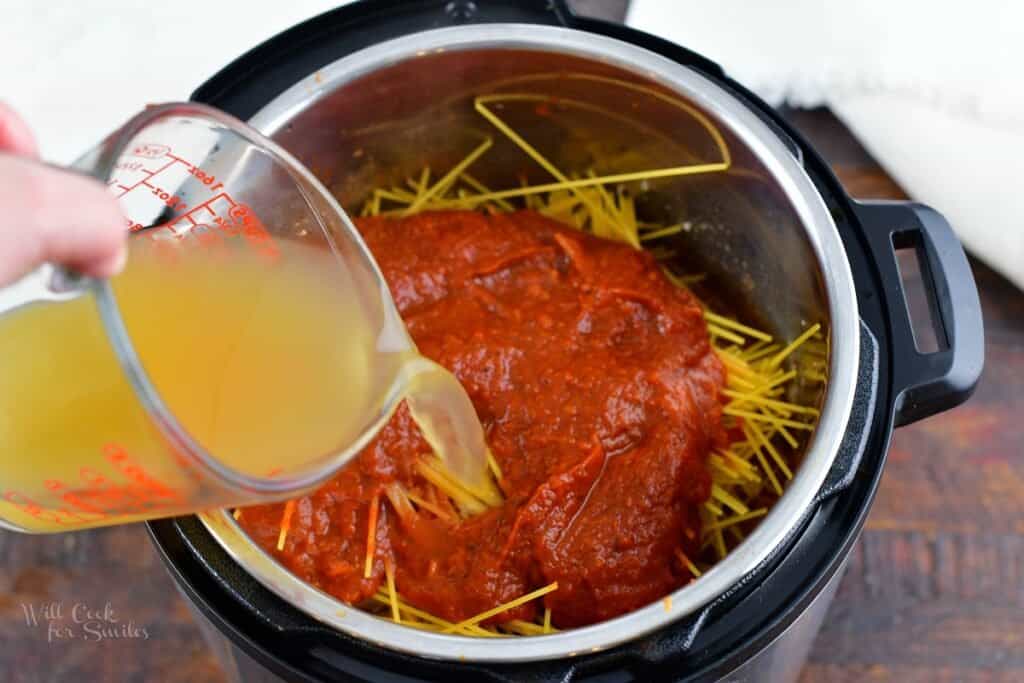 pouring in chicken stock into the pot with spaghetti and sauce