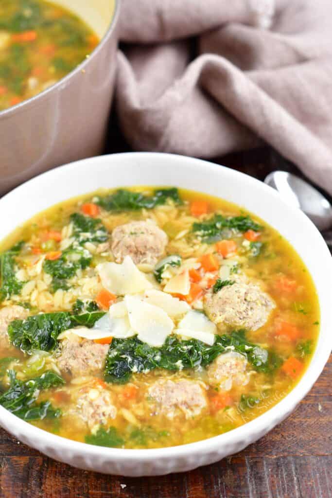 Italian wedding soup in a white bowl topped with shaved parmesan